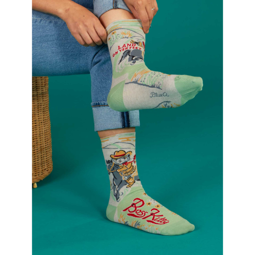A pair of Blue Q socks featuring a confident cartoon cat with the phrase "Boss Kitty," designed with fun colors and a sassy vibe for strong, independent personalities.