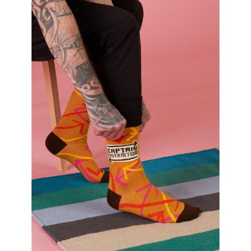 A colorful pair of Blue Q socks featuring the phrase 'Captain Distraction' with fun superhero-style graphics, perfect for easily distracted but lovable personalities.