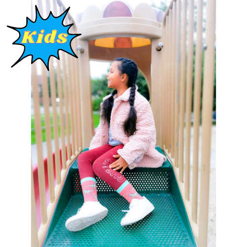 CLASSIC JURASSIC SOCKS - KIDS'. Pink background with t-rex pattern all over the socks. Teal toes and top of socks with lime green heal.
