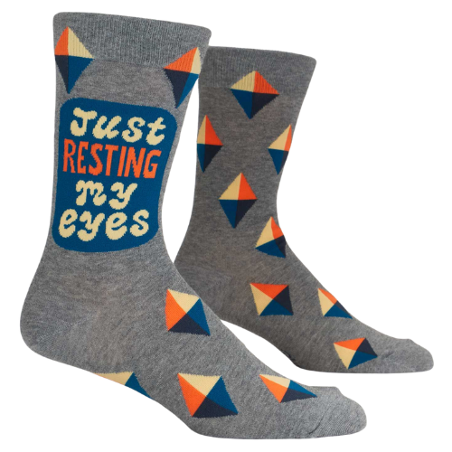 Blue Q men’s socks with the phrase ‘Just Resting My Eyes’ and a cartoon-style character lounging with eyes closed, in bold, playful design.