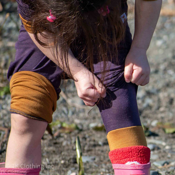 Child outdoors in TK Clothing handmade merino leggings, adjusting pant leg, beach setting