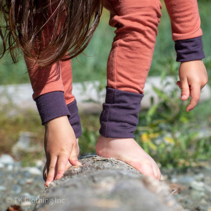 Child balancing barefoot on a log outdoors, wearing handmade TK Clothing merino wool base weight thermals