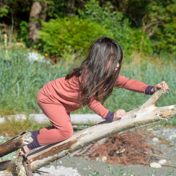 Child in pink and purple trim merino wool thermal set made by TK Clothing Inc climbing driftwood outdoors