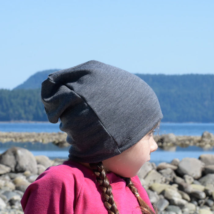 Child on a beach wearing a charcoal merino wool slouchie hat made by TK Clothing