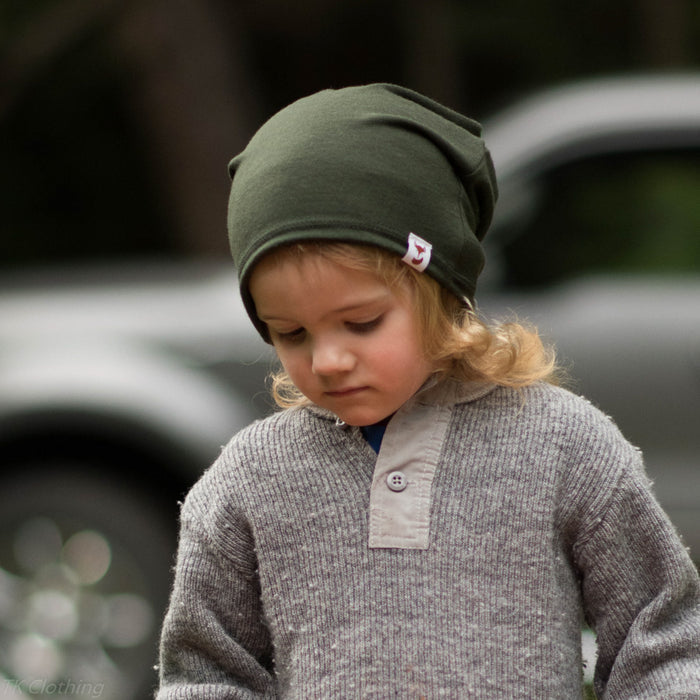 Child in a yard wearing a dark olive green merino wool slouchie hat made by TK Clothing