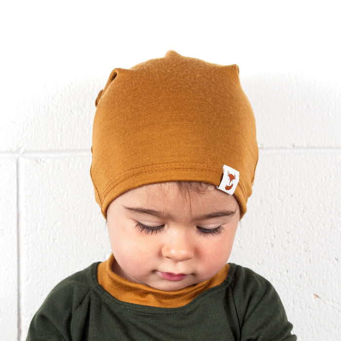 Toddler wearing the ochre merino wool slouchie hat made by TK Clothing. Has on matching merino wool base layer set