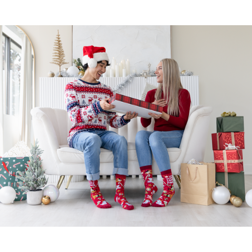 Two people sitting on a couch wearing matching Christmas-themed socks and sweaters, surrounded by holiday decorations.