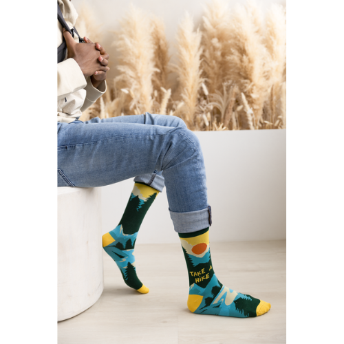 Pair of green, teal, and yellow men's crew socks with a mountain and sun design, featuring the phrase 'Take A Hike' on the side.